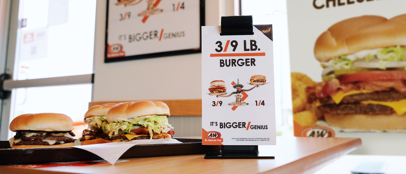 Photo of two burgers sitting on a table in an A&W Restaurant. A table tent that says 